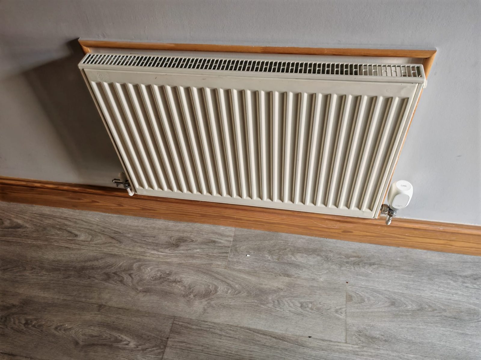New radiator installed against fresh wood flooring
